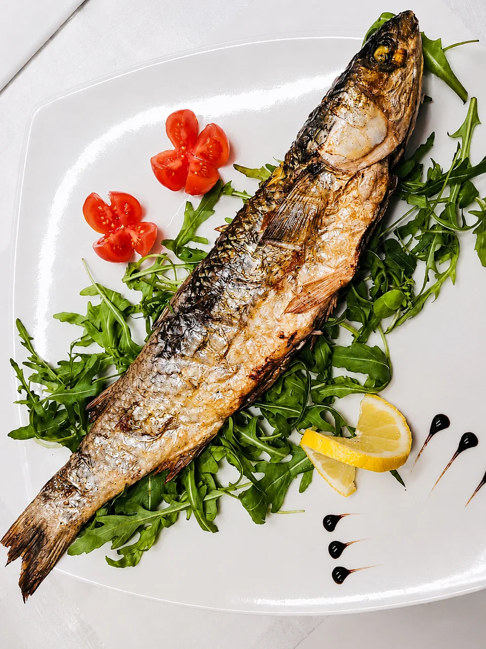 Pesce arrostito intero servito con rucola e limone